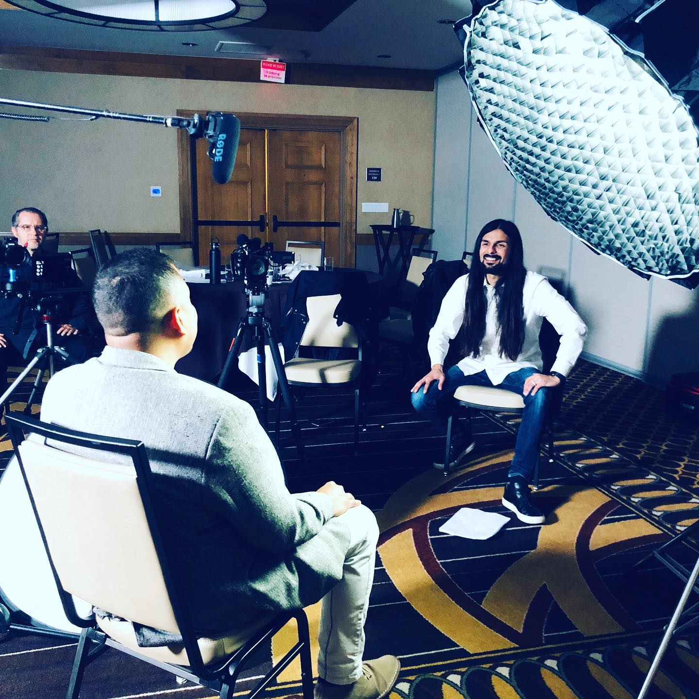Chris Olivarez smiling during an interview, with cameras, crew and lighting visible