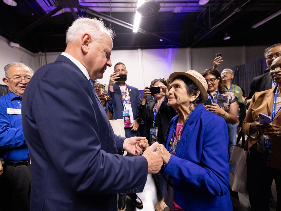 Labor leader Dolores Huerta and Minnesota Governor Tim Walz holding hands in conversation among convention attendees