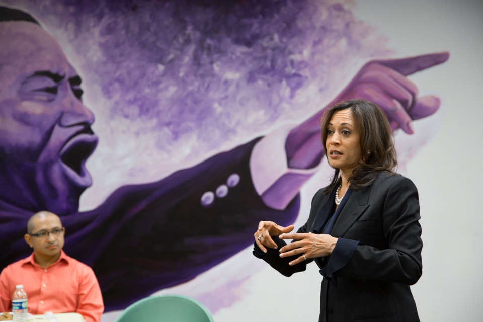 California Attorney General Kamala Harris speaking in front of a mural of Martin Luther King Jr. in 2013